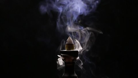 Aromatic cone smoldering in a ceramic stand and emits smoke of different colors and intensity
