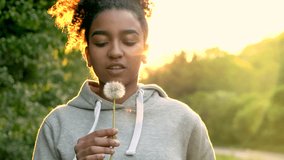 4K video clip of beautiful happy mixed race African American girl teenager girl young woman laughing, smiling and blowing a dandelion at sunset or sunrise