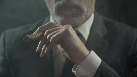 Rich male in suit enjoying process of smoking expensive cigar, slow-motion