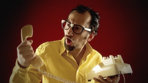 A funny ugly nerdy man dialing a number and talking on a vintage retro rotary phone, getting worried and saying a big no before closing the conversation.
