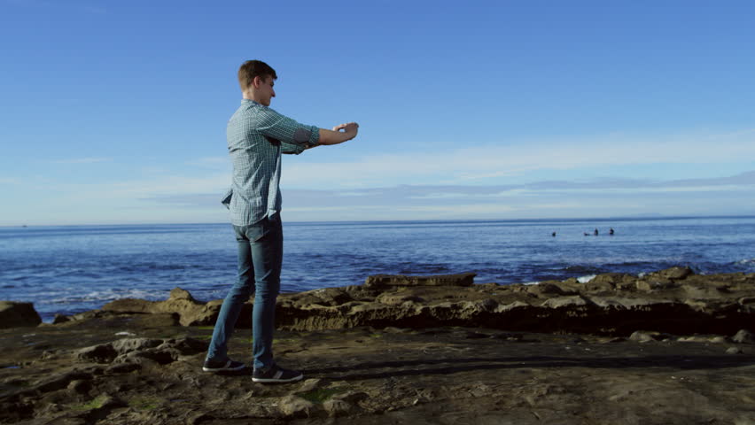 Young attractive man is shooting a video on a beach over his smartphone