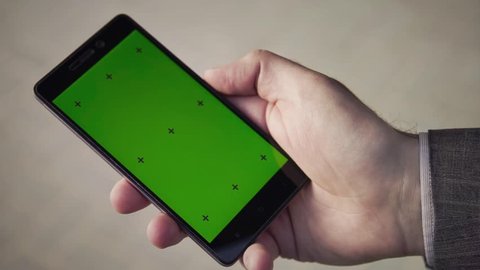 The hand of a businessman who keeps a smart-phone. Sleeve jacket and shirt parts. Green screen. Click on the screen of the mobile phone. Switches the mobile app with a finger on the smartphone