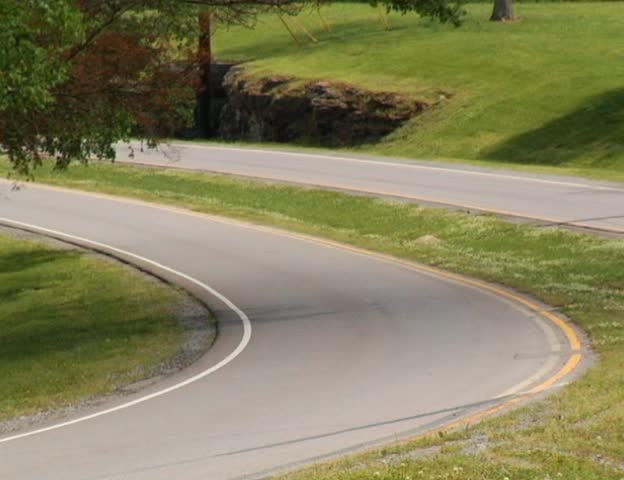 A police car turns around the corner of a rural road during the day PAL video