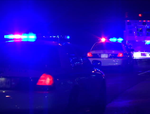 Two police cars and an ambulance flash their lights at night while parked on the side of the road. DV NTSC video