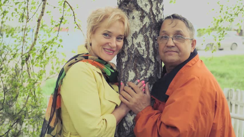 Adult couple in love standing near birch, posing, husband kissing his wife