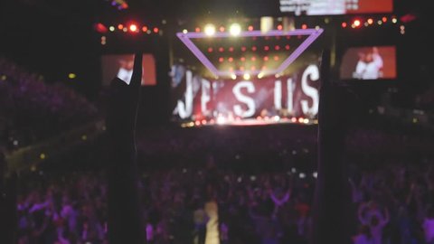 Anonymous woman with arms up at christian concert  worshiping to the God in crowd of people. Slow motion footage. Focus on hands.