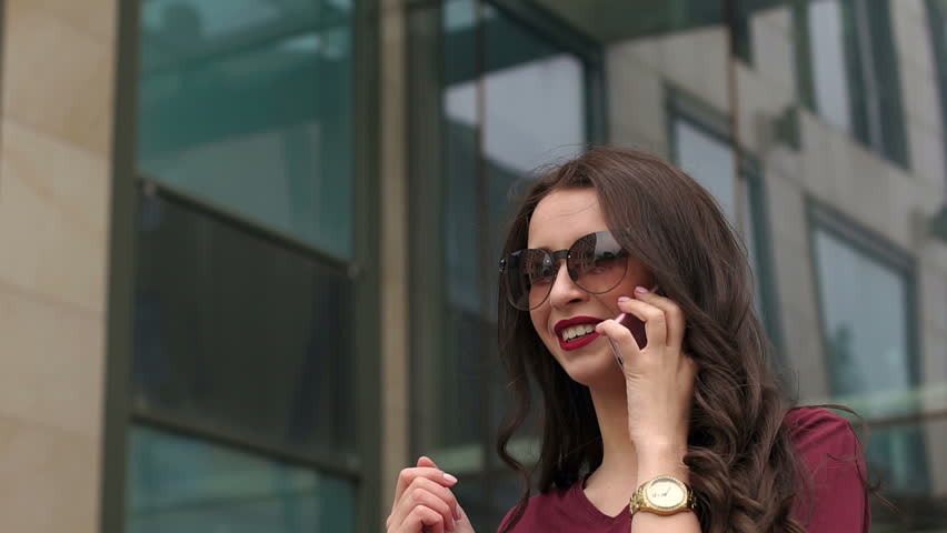 Girl hipster in a red t-shirt with the phone on the background of modern glass building close up. Slow motion. Royalty-Free Stock Footage #27107671