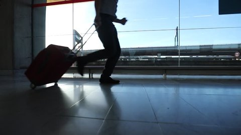 slow motion of business man traveler running in hurry in the airport, silhouette of legs and baggage of passenger