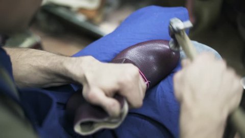 Top view of a shoemaker hammering a purple leather shoe with a pink lace and putting it away when the job is done. Handheld real time close up shot