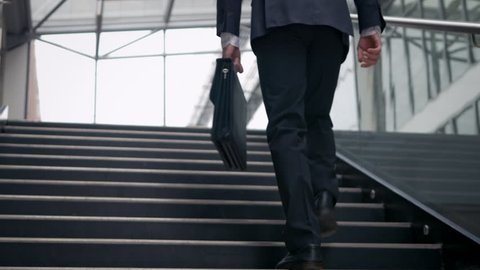 Businessman climbing up the stairs in the building. Confident man dressed in suit on a his successful career path. Low angle shot.