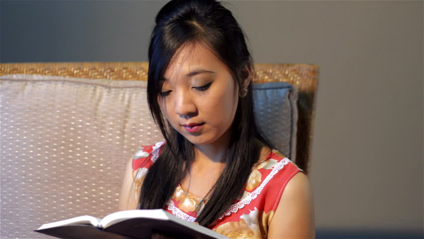 Young Asian woman relaxing on a chair, reading the bible/ a book.