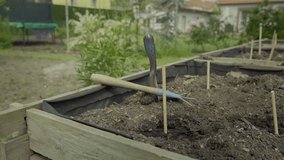 Vegetable elevated wooden beds. Digging hole and planting seeds. Gardening equipment for home gardeners. Trowel, rake and seed setting. Sunny day, agriculture equipment. V-log slow motion footage