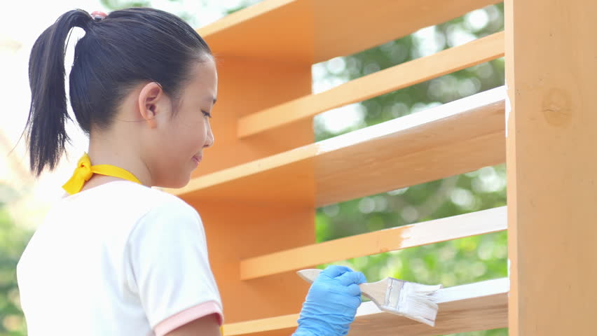 Beautiful Asian girl painting wooden shelf by brush outdoors