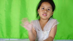 Little asian girl waving her hand saying goodbye on green background,