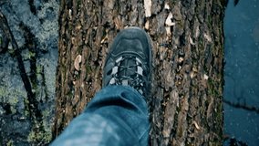 Slow motion of view from above on feet of a person in boots and jeans walking on fallen tree trunk in a river, lake or pond