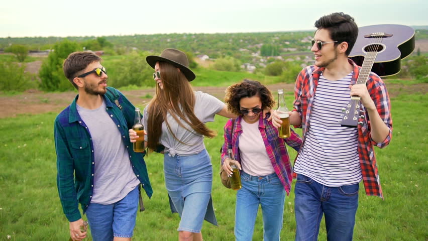 Group of happy hipsters walks forward int the park with great landscape. They very carefree, carrying bottles of beer and guitar Royalty-Free Stock Footage #27135604