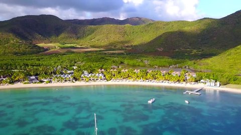 An Aerial video shot with a drone of some luxury resort and beach in Antigua, The Caribbean with blue water and mountains in the background on a sunny day with blue sky and sailboats in the sea