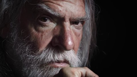 Old man with long white beard looks threatening the camera,darkness