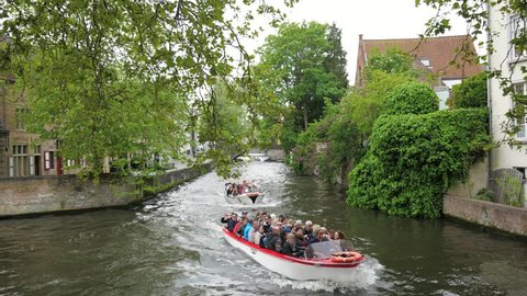 Belgium, Bruges, 03 may 2017. Boats sail along the river channel with the tourists in the old town in cloudy cold weather.