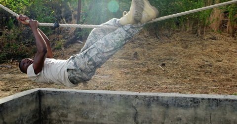 African-american military soldier climbing rope during obstacle course in boot camp
