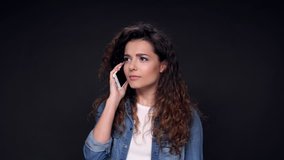 Serious Pretty Curly Woman talking by her smartphone over black background