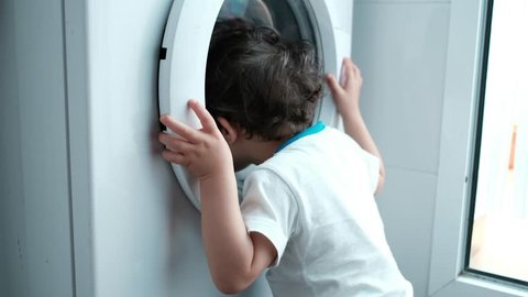 baby two years old boy looking washing machine at home in spin washing program. Home appliances issues.