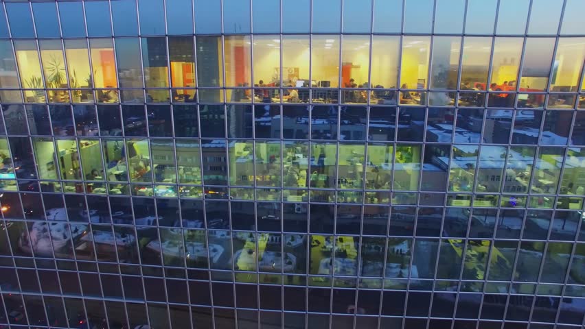 MOSCOW - FEB 16, 2017: People work in offices behind windows with reflection of city at winter evening. Aerial view