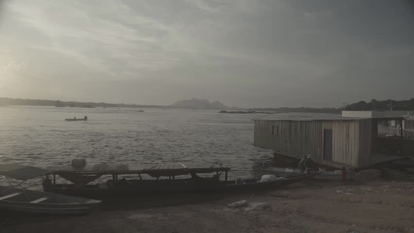 Late afternoon on the Amazon River. A small house on the water and a small boat passing in the background. Scene shot in s-log, with the Sony A7SII, for image processing.