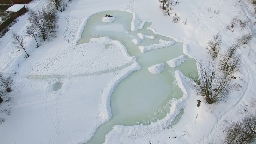 Icy pond covered by snow at winter day. Aerial view