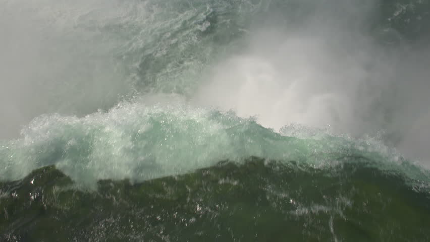 AERIAL TOP DOWN CLOSE UP: Flying above the raging whitewater river dropping over the steep cliff of Niagara Falls crashing on the rocky bottom. Rainbow arc over violent, misty, foamy Horseshoe Falls