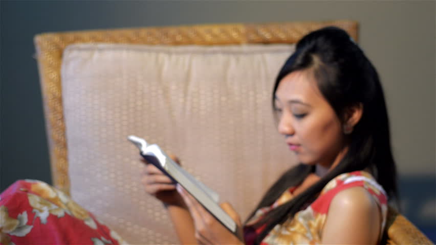 Young Asian woman relaxing on a chair, reading the bible/ a book.