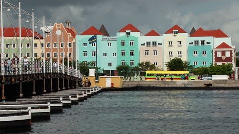 WILLEMSTAD/NETHERLANDS ANTILLES - 11 DECEMBER 2010: The Queen Emma Bridge and pretty colourful buildings in Willemstad Curacao. Taken early morning with people walking across the bridge