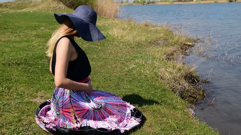 Pregnant girl sitting on the shore and holding her belly