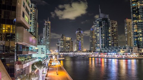 Vew of Dubai Marina promenade with yachts and modern Towers with restaurants from bridge in Dubai night timelapse hyperlapse, United Arab Emirates. 