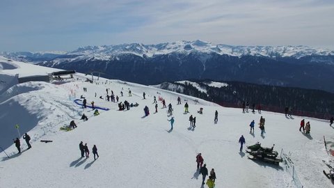 Panorama of ski base on mountain top with crowd of tourists at spring sunny day. Aerial view