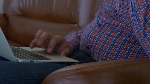 A Man In A Plaid Shirt Sitting On The Leather Couch With the Laptop