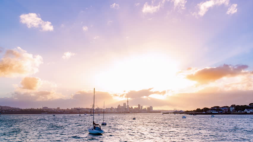 sunset above Auckland city’s skyline with the harbour, the ocean and some boats at the front