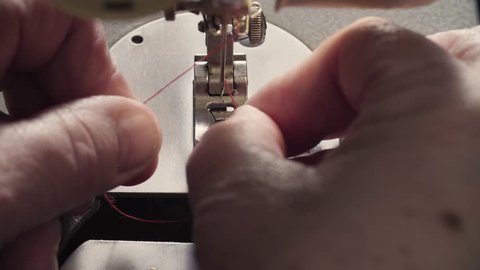 Extreme close up of the hand inserting a thread into a sewing machine needle