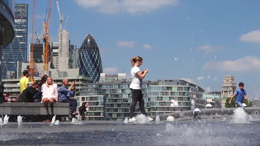 LONDON, UK - 25 MAY 2017:   Tourists bask in the sun by water fountains near the Thames on a hot sunny day