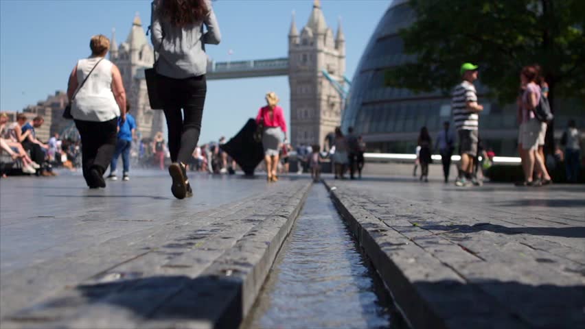 LONDON, UK - 25 MAY 2017:   Tourists and workers cross ‘the rill’ - a man made stream by Tower Bridge on a hot sunny day. Focus on foreground water