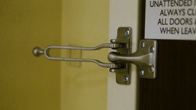 Short clip of a woman's hand securing a hotel room door's deadbolt lock. A ring is visible on one of her fingers. There is a signage of reminders on the door above the lock. 