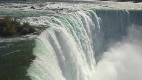 AERIAL CLOSE UP Flying above scenic Niagara Falls along the edge of a cliff. Whitewater rapids breaking and crushing into the bottom of the waterfall. Thick fresh mist rising above the Horseshoe Falls