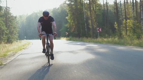 Healthy man doing exercise riding a bicycle outdoors early in the morning. Young and fit cyclist enjoying active lifestyle on an open road in nature. Tracking shot.