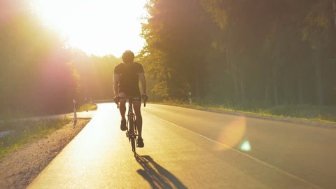 Healthy man doing exercise riding a bicycle outdoors early in the morning. Young and fit cyclist enjoying active lifestyle on an open road in nature. Tracking shot.