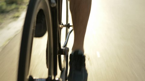 Active male cyclist riding fast on a road bicycle. Tough athlete doing endurance training outdoors. Tracking shot with sun from behind.