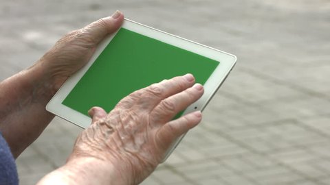 2 Shots. 1. Tablet PC close-up. Green screen. 2. An elderly woman sits on a bench in the park and enjoys a tablet PC. She touches the screen then looks at the camera and smiles.