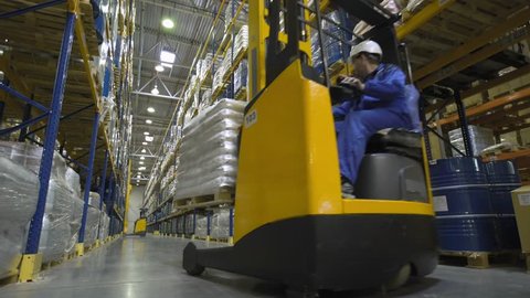 Warehouse worker on stacker loading cargo on rack