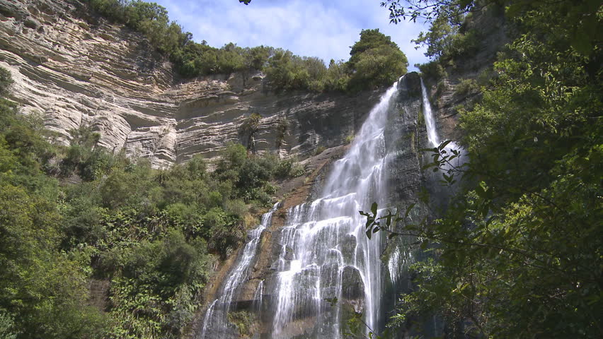Water from a stream cascades down the rocky face of a high waterfall 