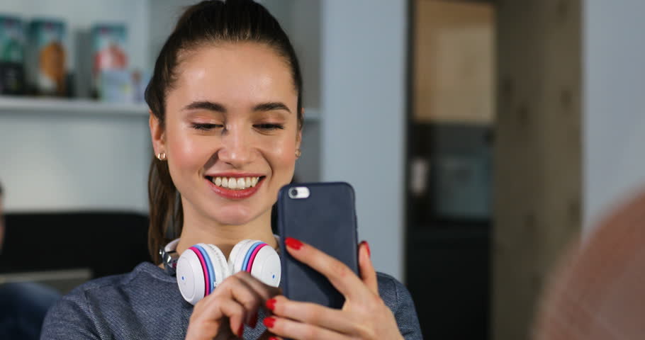 Portrait of a young beautiful woman with headphones makes selfie on phone in the office