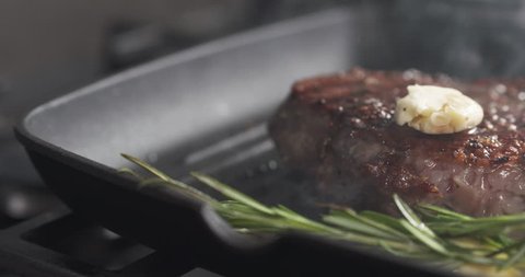Slide slow motion shot of flip rib eye steak with herbs on grill pan, 4k 60fps prores footage